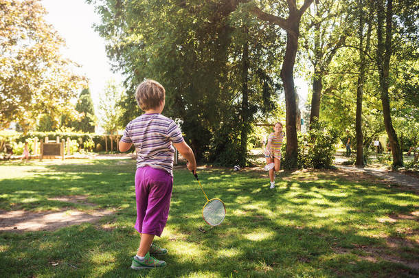 两个有趣的孩子朋友在夏季公园打羽毛球。孩子们在阳光明媚的日子里一起玩