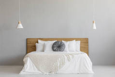 在木床上的针织毯子, 在最小的卧室内部与灯的灰色墙壁。真正的照片与一个地方为您的床头柜