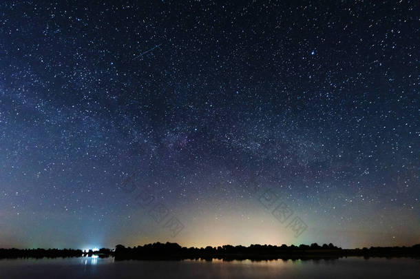 在河岸上的一个迷人的星夜，有一棵大树，天空中的一条银河，夏天有流星坠落.
