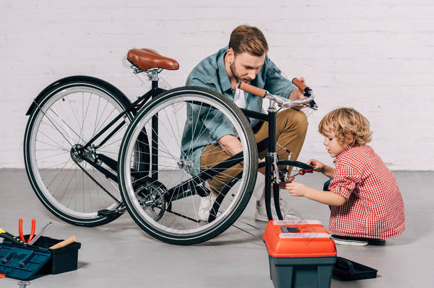 在车间里, 帮助小男孩在工具箱里的工具箱附近修理自行车的男子