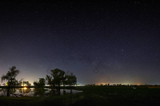 夜空中有银河系的星星的空间。与河和树的风景被拍照在长的曝光.