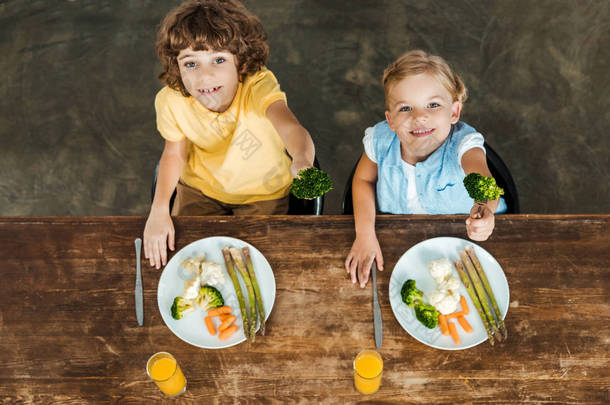 高角度看可爱快乐的孩子拿着叉子与花椰菜和微笑在照相机