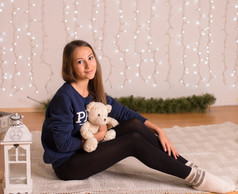 beautiful young girl in a sweatshirt and tights near the Christmas tree, Christmas lights in the bac