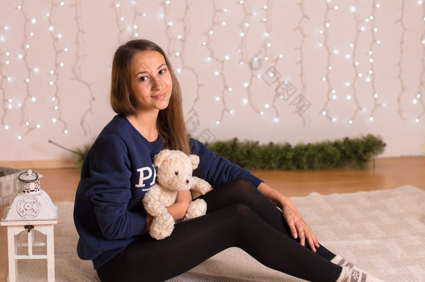 beautiful young girl in a sweatshirt and tights near the Christmas tree, Christmas lights in the bac