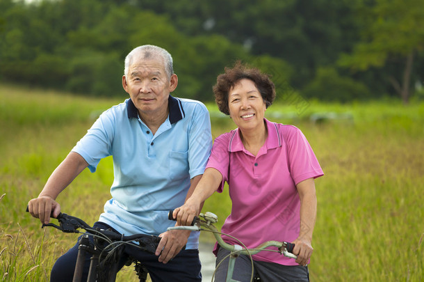 快乐的<strong>亚洲</strong>老年人对夫妇在公园里骑自行车.