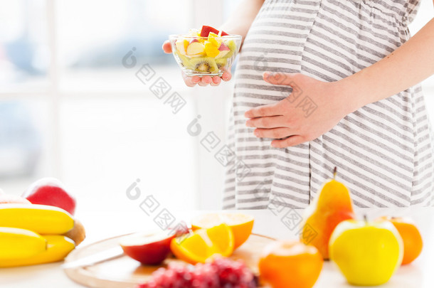 怀孕的妇女抱着水果沙拉