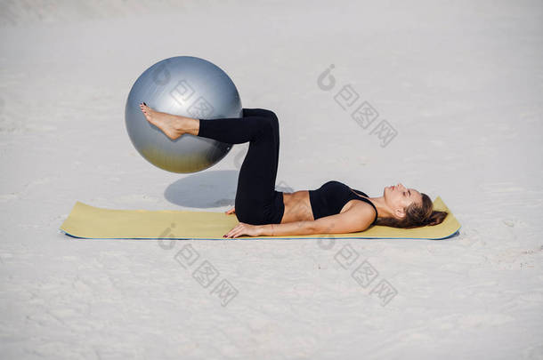 体育和健康的生活方式概念。美丽的<strong>健身</strong>女孩做胃锻炼与合适的<strong>球</strong>在海滩上。做普拉提锻炼的年轻妇女.