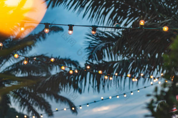 模糊光散景与椰子棕榈树背景日落, 黄色串灯与散景装饰在户外餐厅