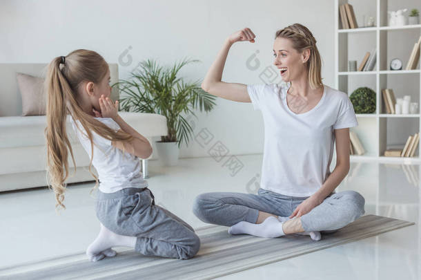 母亲在家里向女儿展示二头肌肌肉