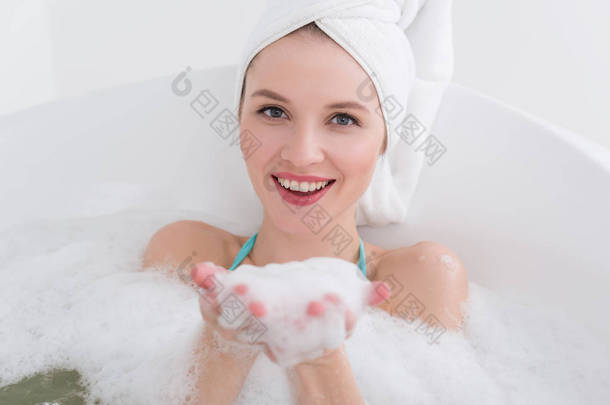 微笑的妇女与毛巾在头放松在<strong>浴</strong>与泡沫在温泉沙龙