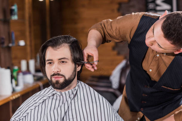 英俊的年轻人得到理发从专业理发师在理发店