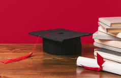 以红色为文凭和学术帽的一堆书的裁剪图像