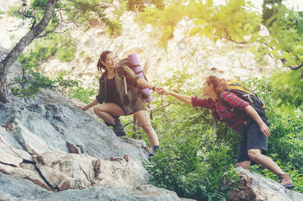 团体远足妇女帮助她的<strong>朋友</strong>爬上落山的最后一段。旅行团团队精神走在户外生活冒险和露营中.旅行概念.