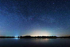 在河岸上的一个迷人的星夜，有一棵大树，天空中的一条银河，夏天有流星坠落.