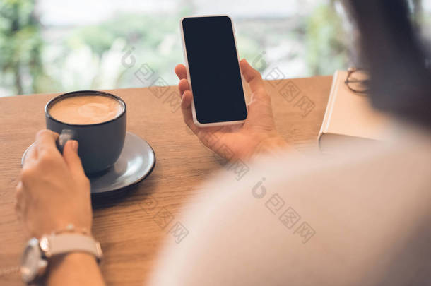 咖啡杯用智能手机在咖啡馆里的女人的部分看法