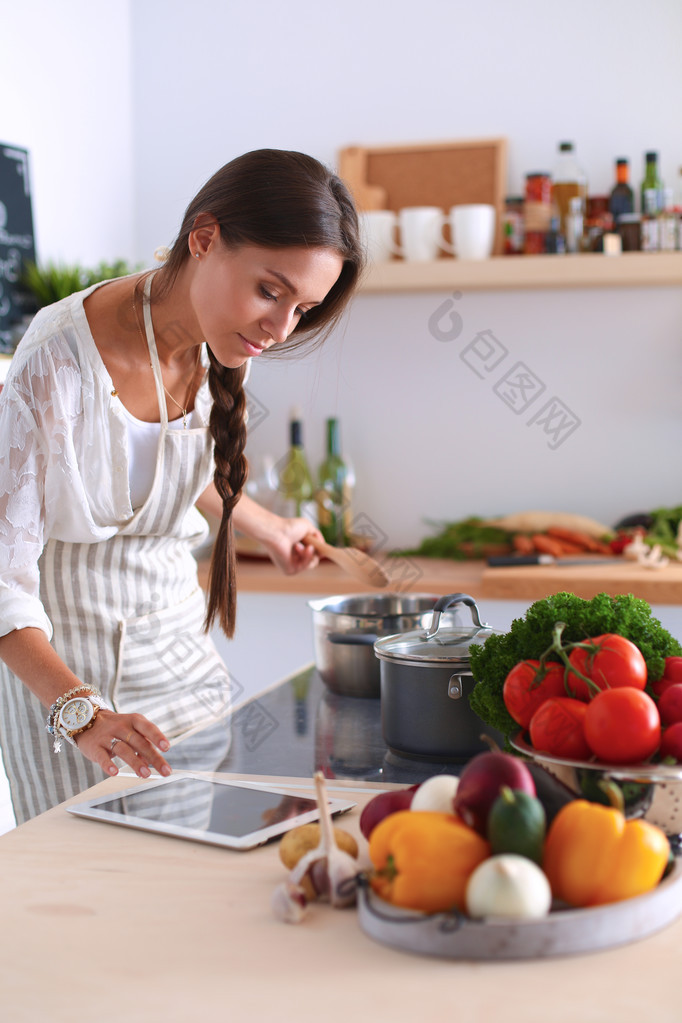 年轻女人在厨房里用平板电脑做饭