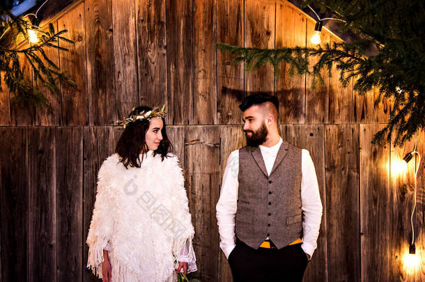 新婚夫妇、新娘和新郎，背景是一座古老的木制房子和复古的花环.