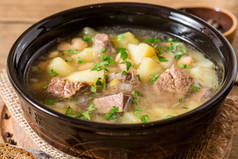 土豆、 豆类和韭葱石背景上的陶瓷碗里的牛肉汤.
