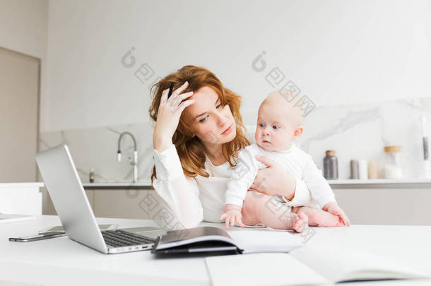 一个体贴的商业妇女的肖像抱着她的小宝宝, 而坐在桌子和工作隔离