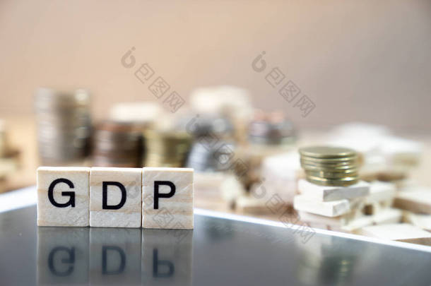 在木立方体中书写的 Gdp 词在黑色 mirrow 上的反射以货币栈为背景图