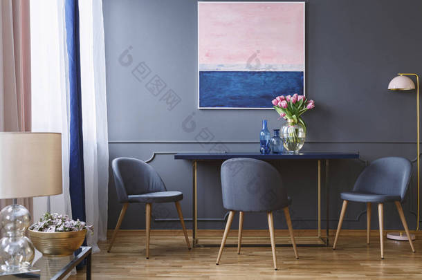 桌上有粉红色的花朵, 里面有油漆和灰色的椅子, 旁边是台灯。真实照片