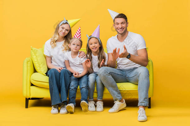 戴着生日派对帽<strong>的</strong>快乐家庭在黄色<strong>的</strong>沙发上欢呼