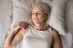 健康安详成熟的女人一个人睡在床上，俯瞰全景