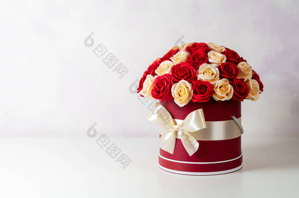 一束粉红色和白色的玫瑰装饰在一个帽子盒上的光背景.