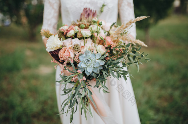 新娘穿着婚纱站在一个绿色的花园，手里拿着一束<strong>鲜花</strong>和绿叶