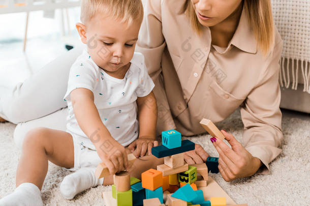 可爱的幼儿玩五颜六色的立方体和母亲在托儿所房间的裁剪视图
