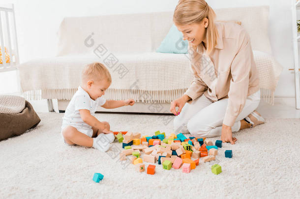 可爱的幼儿玩五颜六色的立方体和母亲在托儿所室