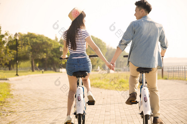 快乐的年轻夫妇，骑着自行车在城市公园