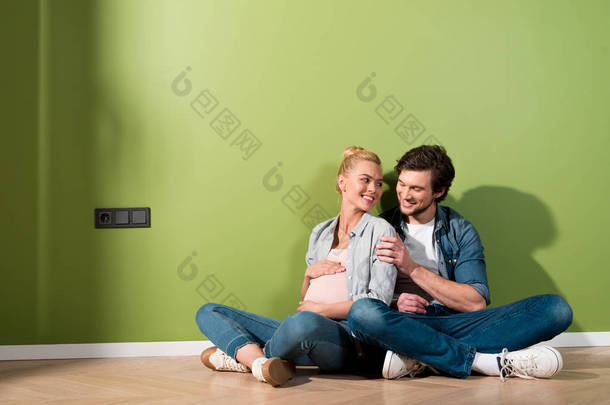 微笑的男人坐在地板上, 拥抱怀孕的妻子