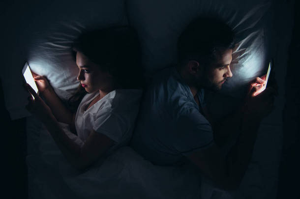 夫妇背靠背躺在床上, <strong>晚上</strong>使用智能手机