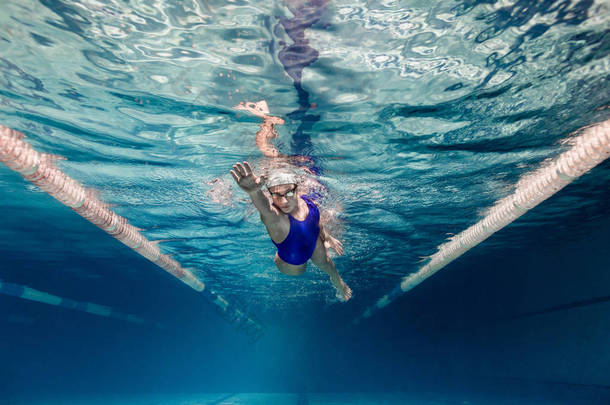 游泳衣中女游泳运动员的水下图片及泳池的护目镜训练