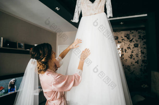 年轻美丽的新娘看她的婚纱礼服 