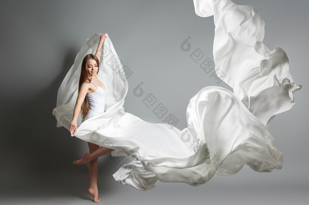 美丽的年轻姑娘跳舞。中飞白色连衣裙的女孩。白色的布料在空中飞翔。白色的光穿衣服