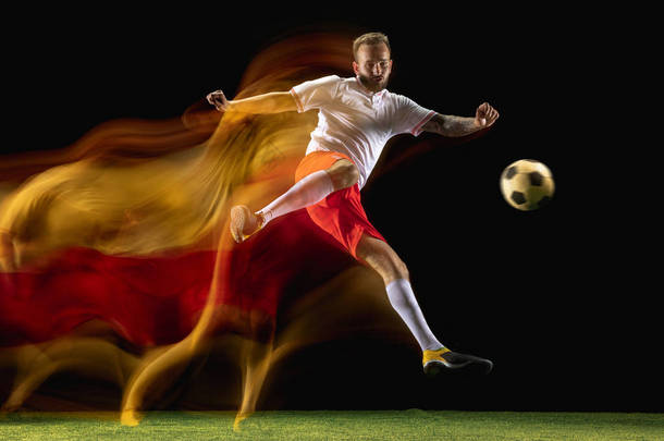 男子足球运动员在混合光的黑暗背景踢球