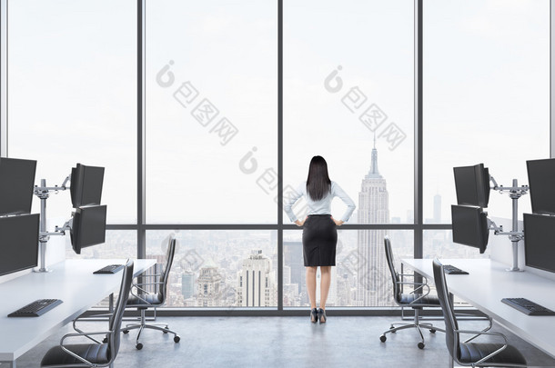 Rear view of a lady in formal suit who is looking out the window in the modern panoramic office with