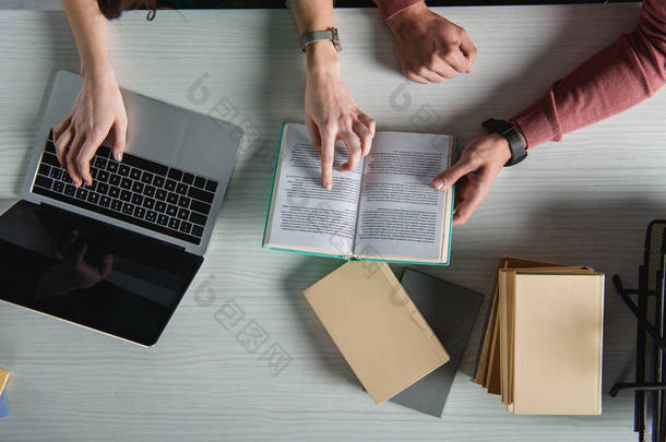 笔记本电脑的顶部视图与空白屏幕靠近妇女用手指指着书在男子附近 