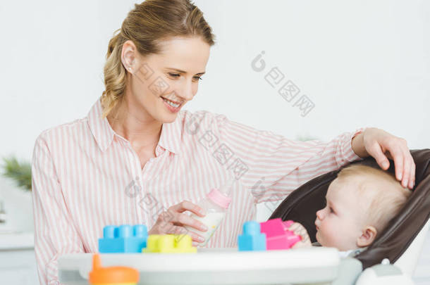 母亲带奶瓶和<strong>婴儿</strong>的女儿坐在<strong>婴儿</strong>椅与塑料块