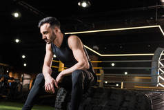 运动男子坐在运动轮胎在健身房的低角度视图 