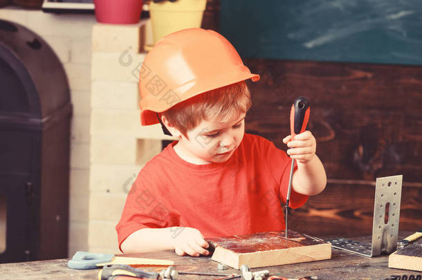 童年的概念。男孩在橙色硬帽子或头盔, 学习室背景。孩子梦想未来的建筑或建筑事业。男孩扮演建设者或修理工, 使用工具