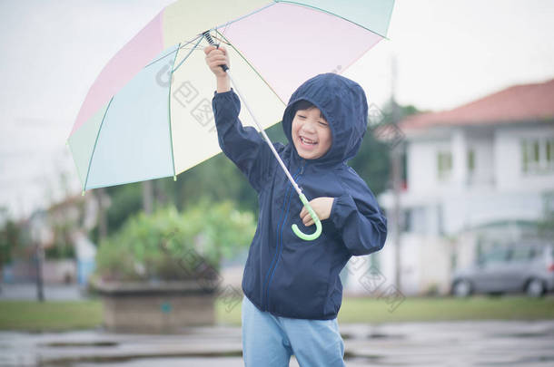 快乐的亚洲男孩抱着五颜六色的伞，公园里玩 
