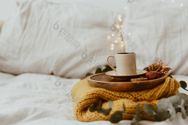 咖啡杯放在木托盘和温暖的毛衣与<strong>背景</strong>散景模糊的灯光。早上在床上。仍然生活构成以拷贝空间 