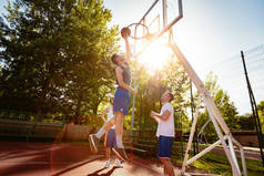 年轻的篮球运动员在街头球场进行训练。他们在一起玩耍和行动。年轻人投掷球到圆环. 