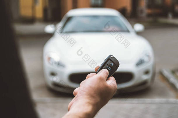男人用钥匙链打开车，背景是一辆白色汽车.