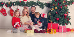 拥有圣诞礼物的快乐家庭坐在装饰过的圣诞树旁
