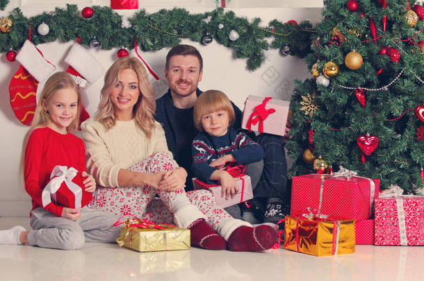 拥有圣诞礼物的快乐家庭坐在装饰过的圣诞树旁
