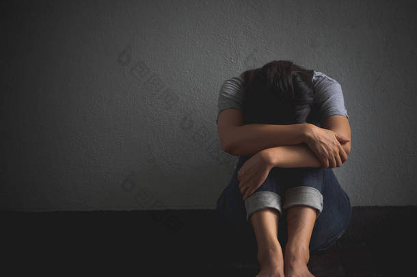悲伤的女人抱着她的膝盖和哭泣。悲伤的女人独自坐在空荡荡的房间.